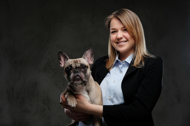 Portrait of a smiling blonde woman breeder holds her cute pug. Isolated on a dark textured background.