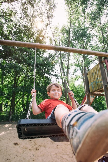 Photo portrait of smiling boy sitting on swing at playground