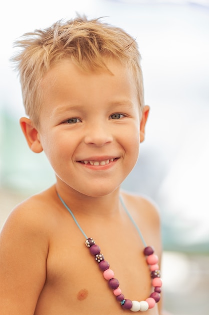 A portrait of a smiling boy, wearing a purple necklace