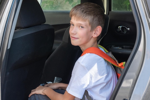 Portrait of a smiling boy with a school bag sitting in a car The happy child was brought to school by car Back to school concept