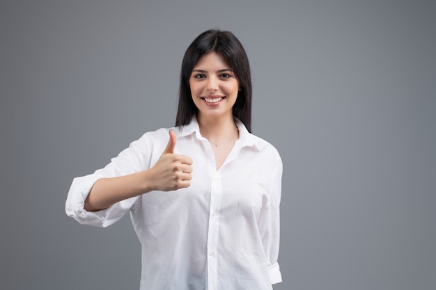 Portrait of a smiling business woman freelancer showing thumb up isolated over grey