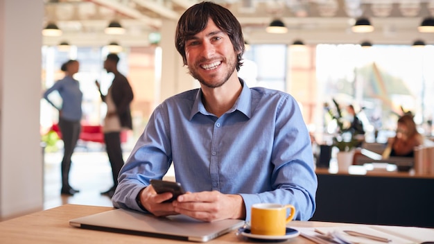 Portrait Of Smiling Businessman Sitting At Desk With Laptop In Modern Open Plan Office