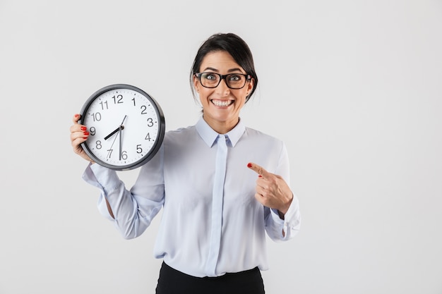 Portrait of smiling businesswoman wearing eyeglasses holding round clock in the office, isolated over white wall