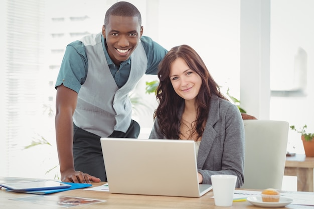 Portrait of smiling businesswoman working on laptop with coworker at desk 