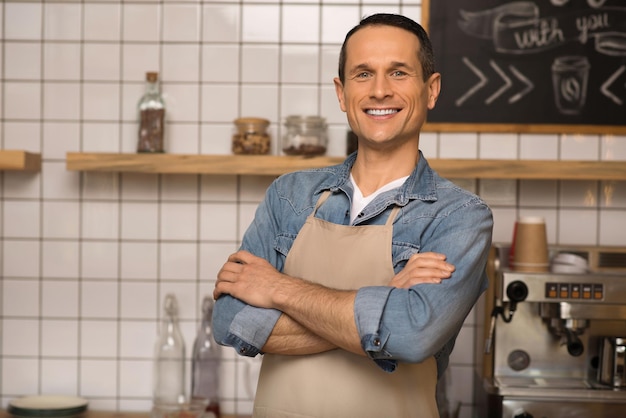 Portrait of smiling cafe owner with crossed arms standing in coffee shop