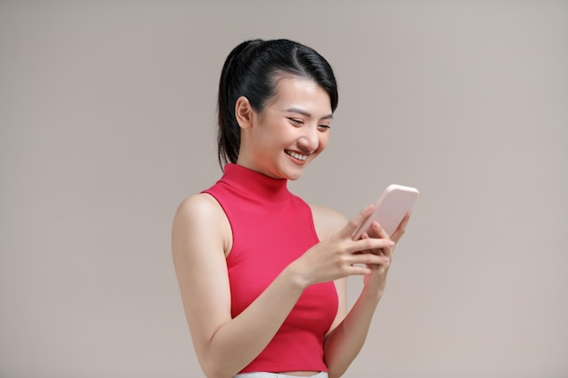 Portrait of a smiling casual woman holding mobile phone over beige background