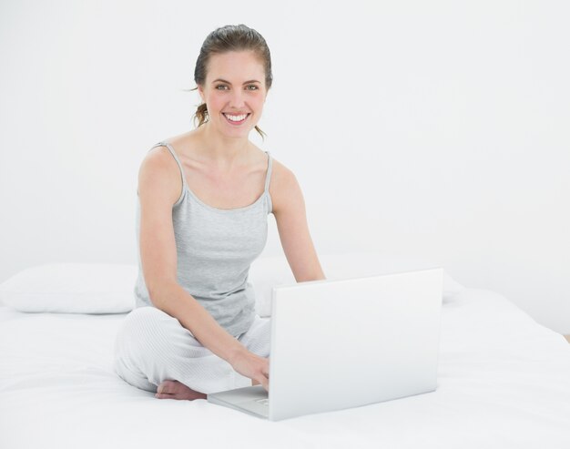 Portrait of a smiling casual woman with laptop in bed