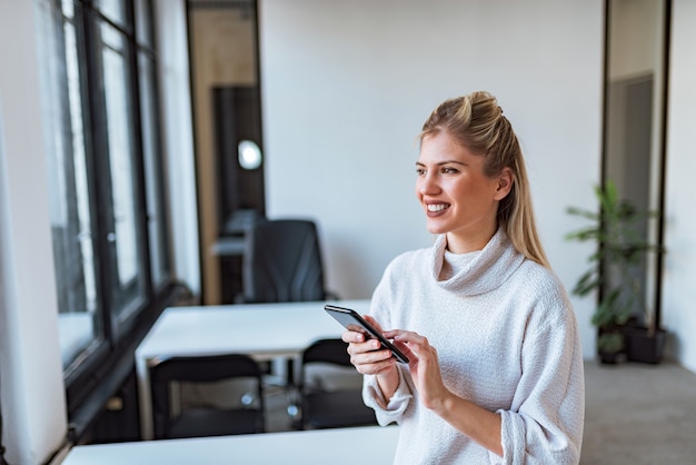 Portrait of a smiling casual young woman with smart phone indoors.