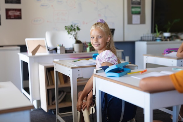 Portrait of smiling caucasian elementary schoolgirl sitting at desk in classroom