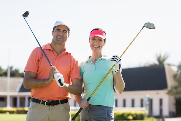 Portrait of smiling couple holding golf clubs