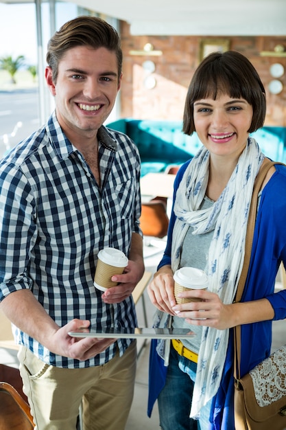 Portrait of smiling couple with coffee cups using a digital tablet