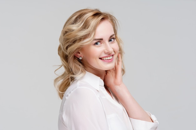 Portrait of smiling curly woman in white shirt isolated on gray background