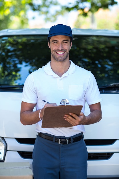 Portrait of smiling delivery man writing in clipboard