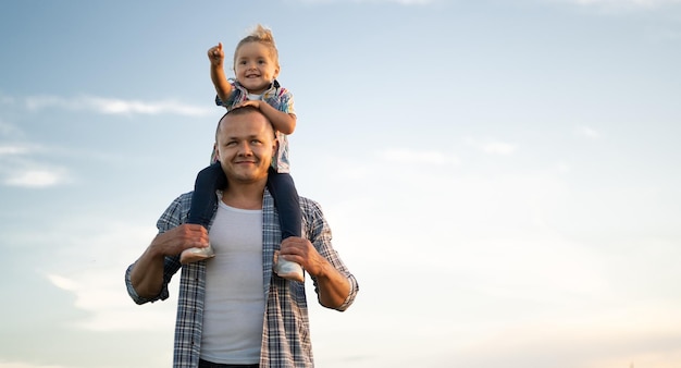 Portrait of a smiling father holding a little Caucasian girl daughter on his shoulders against the backdrop of a sunset sky with clouds standing happy dad with baby Happy family concept