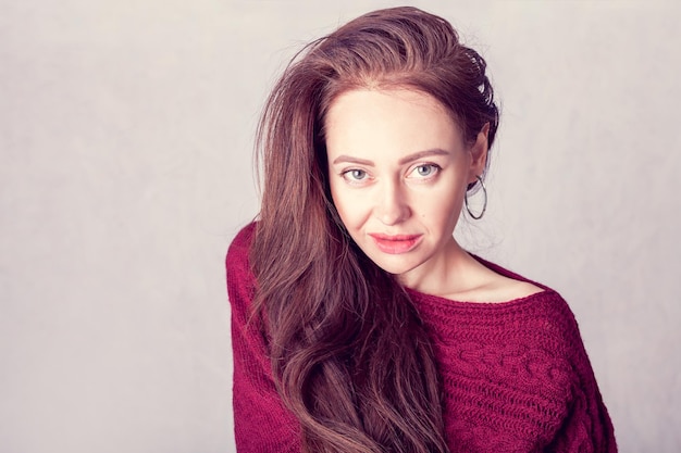 Portrait of a smiling girl in a burgundy knitted sweater with space for note on the background