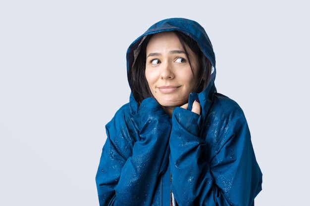 Portrait of a smiling girl dressed in blue raincoat in drops posing with hood on grey