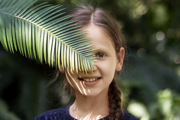 Portrait smiling Girl hiding face palm leaf. People Children Nature concept.