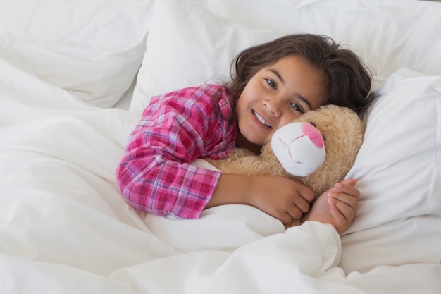 Portrait of a smiling girl with stuffed toy resting in bed