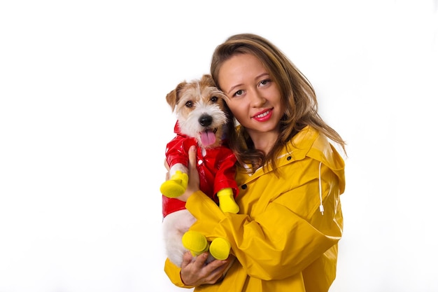 Portrait of a smiling girl in a yellow raincoat with a dog Jack Russell Terrier in a red jacket in her arms. Isolated on white background