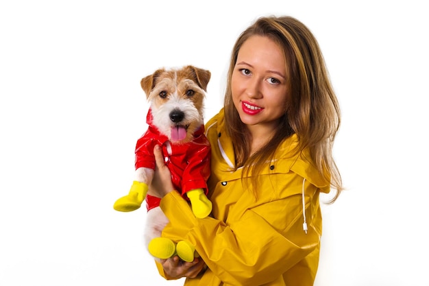 Portrait of a smiling girl in a yellow raincoat with a dog Jack Russell Terrier in a red jacket in her arms. Isolated on white background