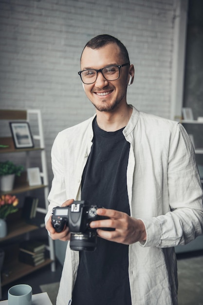 Portrait of a smiling handsome photographer holding camera standing in his studio professional photo