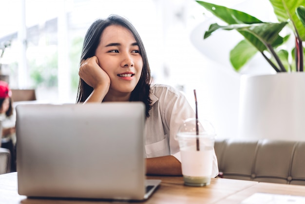 Portrait of smiling happy beautiful asian woman relaxing using laptop computer and looking something while sitting on sofa.