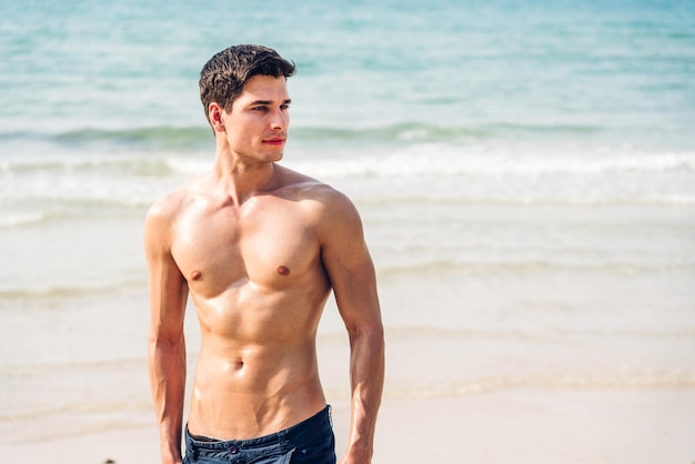 Portrait of smiling happy handsome sexy man showing muscular fit body enjoying and relax standing on the tropical beachSummer vacations and travel