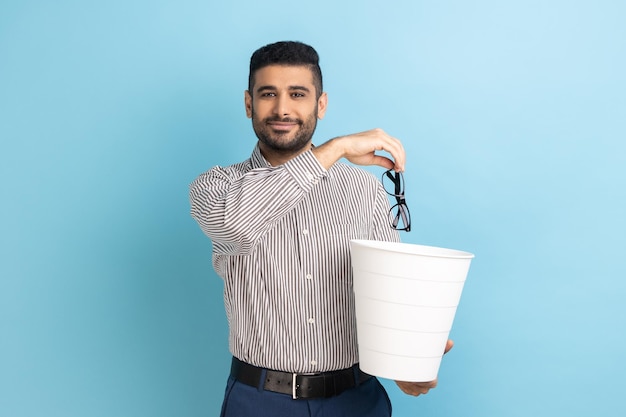 Portrait of smiling happy satisfied businessman throwing out his optical glasses after vision treatment looking at camera wearing striped shirt Indoor studio shot isolated on blue background