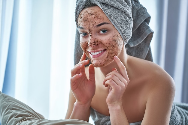 Portrait of smiling happy woman in bath towel with natural face coffee scrub mask after shower