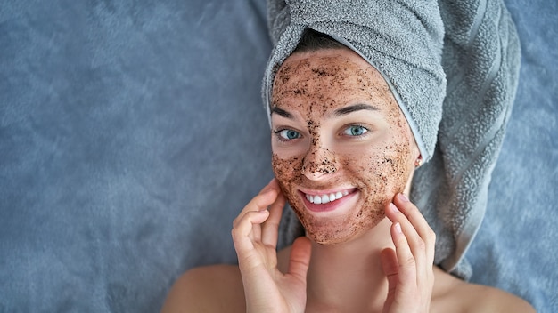 Portrait of smiling healthy female in bath towel with natural cleansing face coffee scrub after shower