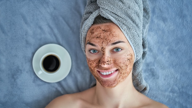 Portrait of smiling healthy happy female with coffee scrub facial mask during spa day and skin care