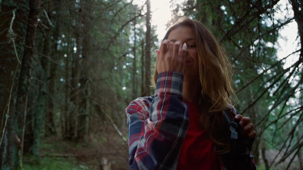 Portrait of smiling hiker looking at camera in fairytale forest Young woman posing at camera outdoor Cheerful tourist wearing backpack Female model with positive emotion