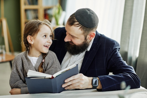 Portrait of smiling jewish father reading book with daughter at home