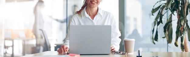 Portrait of smiling lady boss working on laptop at her workplace at modern office