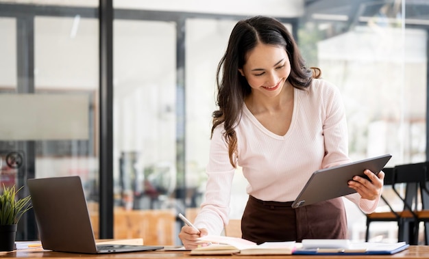 Portrait of smiling lady entrepreneur working on laptop and tablet at workplace in loft office