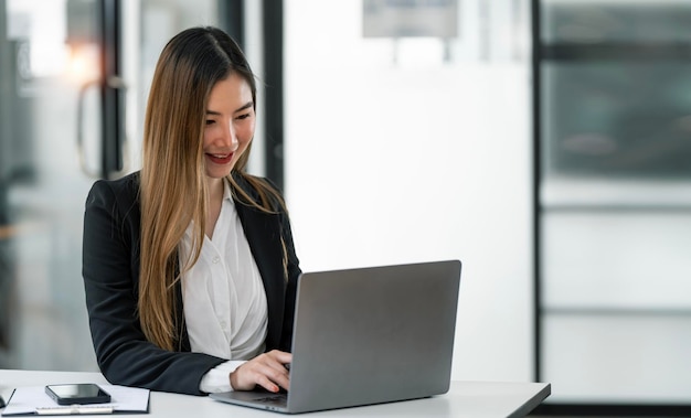 Portrait of smiling lady executive working on laptop at workplace in modern office