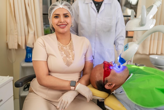 Portrait of a smiling latin female dentist sitting on a clinic next to a patient