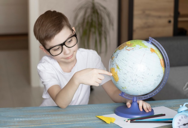 Portrait of smiling little boy sitting at table with his globe