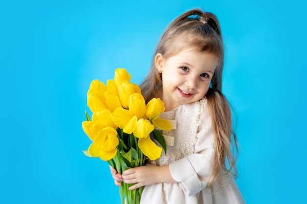 Portrait of a smiling little girl a child with a bouquet of yellow tulips on a blue isolated background Lifestyle International Women's or Mother's Day Space for text Highquality photography