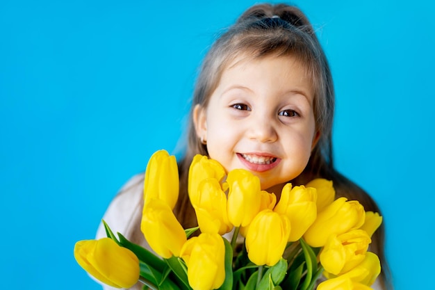 Portrait of a smiling little girl a child with a bouquet of yellow tulips on a blue isolated background Lifestyle International Women's or Mother's Day Space for text Highquality photography