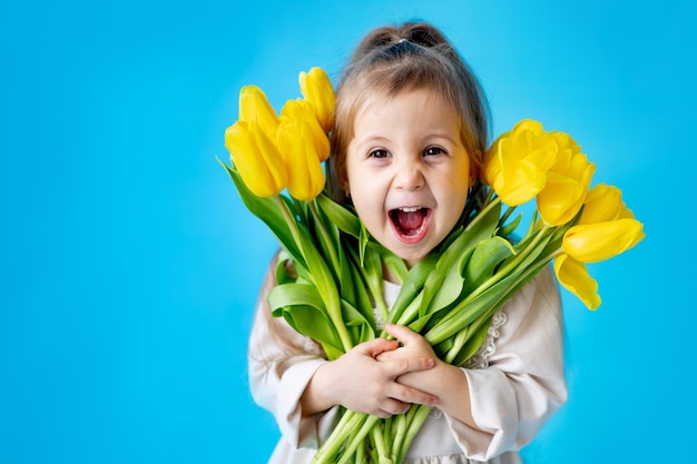 Portrait of a smiling little girl a child with a bouquet of yellow tulips on a blue isolated background Lifestyle International Women's or Mother's Day Space for text Highquality photography