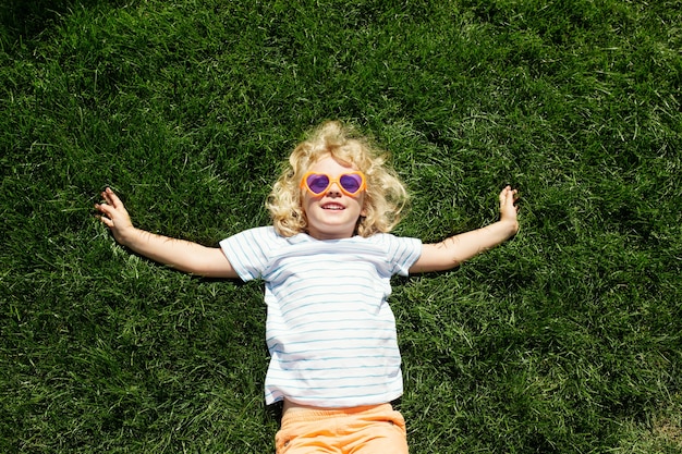 Portrait of a smiling little girl in heart shaped sunglasses lying