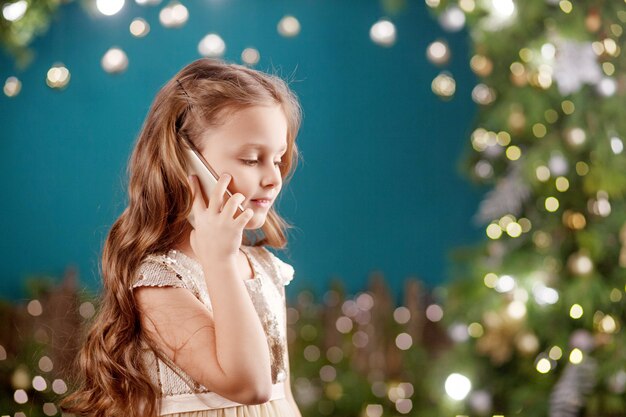 Portrait of a smiling long-haired little girl in dress on  of Christmas lights. Little girl talking on the phone.  New Year and Christmas . 