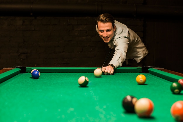 Portrait of a smiling man aiming the cue ball while playing snooker