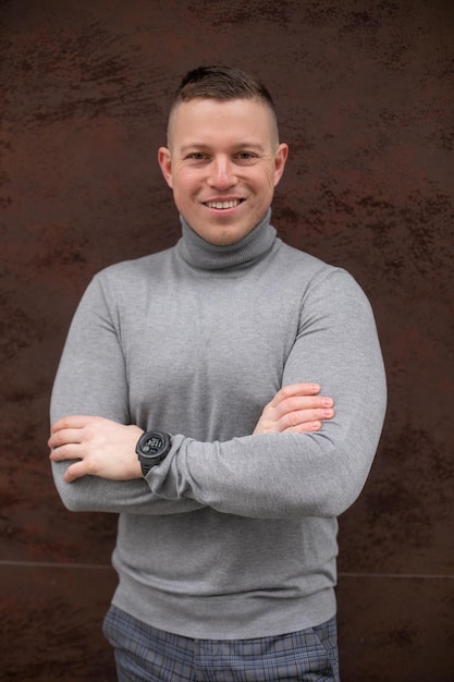 Portrait of smiling man in gray sweater confident stands against wall of city office building Freelance