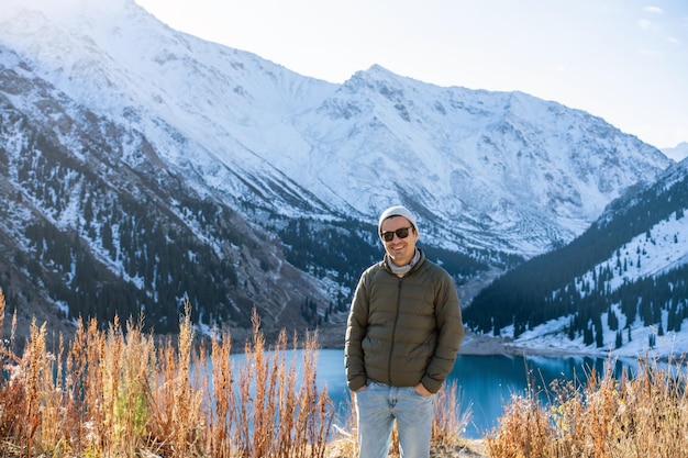 Portrait of a smiling man in sunglasses over lake surrounded by snowy mountians