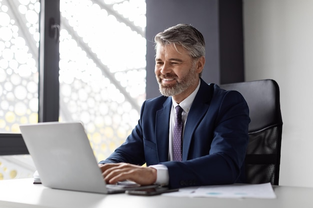 Portrait Of Smiling Middle Aged Businessman Working With Laptop Computer In Office