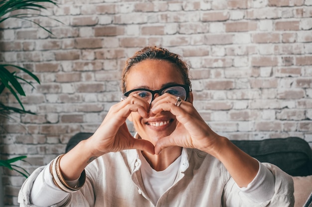 Portrait of smiling millennial Caucasian woman show heart love hand gesture or sign Happy young female look at camera demonstrate support and care feel supportive Volunteer charity conceptxA