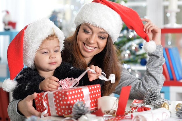 Portrait of smiling mother and cute little daughter preparing for Christmas at home wearing Santa hats