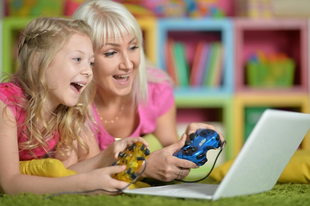 Portrait of smiling mother and daughter using laptop playing video game